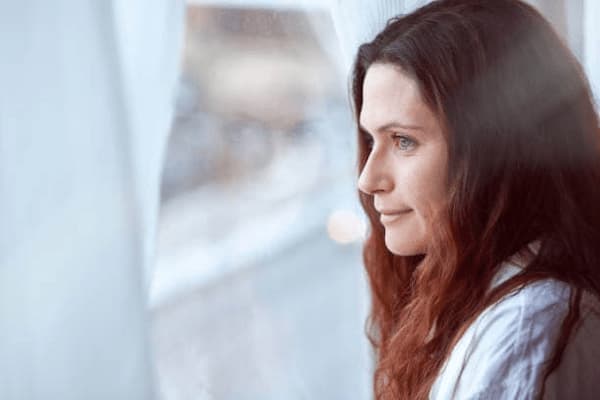 Femme apaisée regardant par la fenêtre, symbole de sérénité et de reconnexion à soi, accompagnement par une sexothérapeute spécialisée dans le désir féminin.